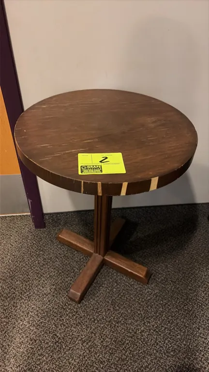 Round wood pedestal table. Features a circular top with decorative edge accents and a central column. 19"Dia. Mounted on a 4-point wood cross base.