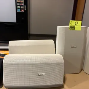 QSC and Tannoy surface-mount speakers. Includes (4) white QSC speakers and (1) black Tannoy speaker. Features perforated metal grilles. Includes mount