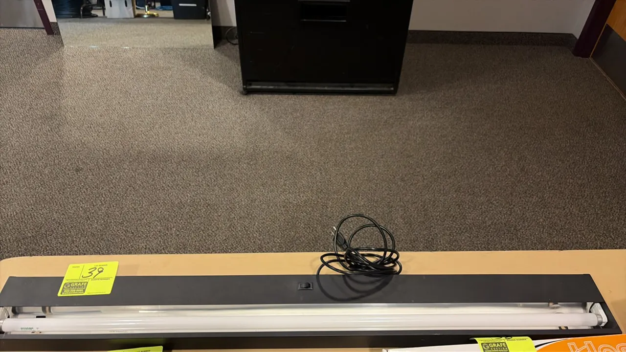 Under-counter task light fixture. Features black housing, integrated rocker switch, installed fluorescent tube, and attached power cord with standard