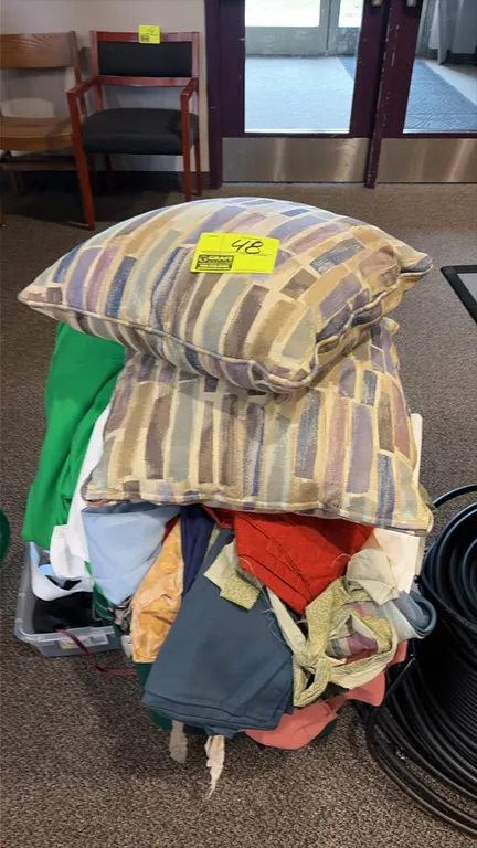Assorted textiles, clothing, and pillows. Includes (2) patterned throw pillows, assorted fabric remnants and linens, and plastic storage containers.