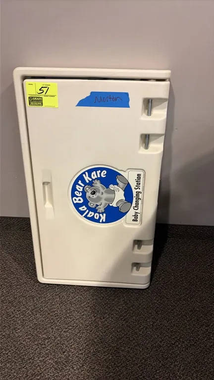 Koala Bear Kare vertical baby changing station. Features fold-down design, integrated child safety strap, and built-in liner dispenser. Molded polyeth