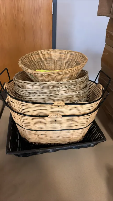 Assorted wicker baskets. Features an assortment of shapes and sizes including round woven display bowls, shallow nested baskets, oval baskets with bla