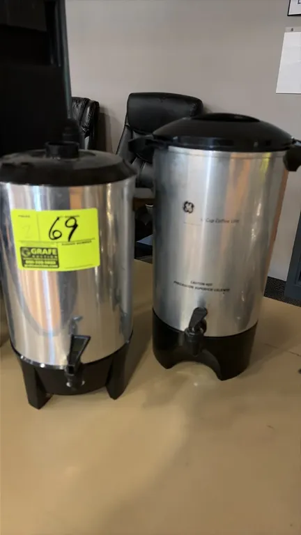 Coffee urns. Includes a GE 42-cup coffee urn and a companion coffee urn. Features aluminum bodies, black plastic bases and lids, dispensing spigots, a