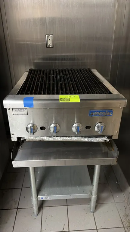 Imperial charbroiler. Features stainless steel exterior, cast iron grates, 4 burner control knobs, and pull-out grease drawer. 24"W. Mounted on a stai