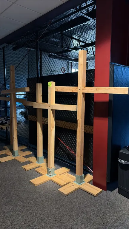 Freestanding wooden display crosses. Constructed from dimensional lumber with horizontal crossbars. Each mounted in a metal post base bracket on a woo