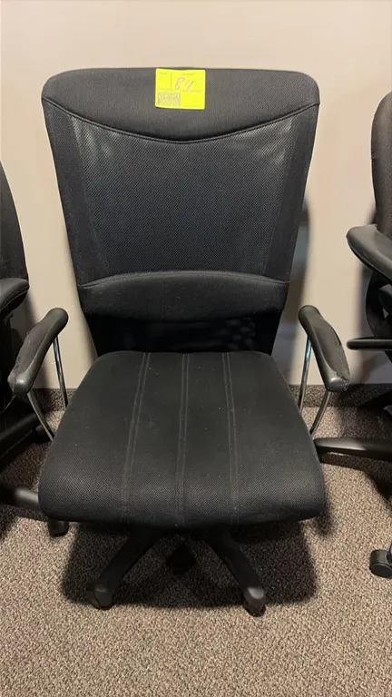 Office chair. Features a black fabric upholstered seat, mesh backrest, and fixed armrests with chrome supports. Mounted on a 5-star base with casters.