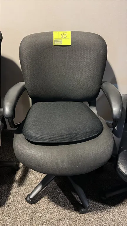 Office chair. Features black fabric upholstery, fixed molded armrests, and an auxiliary seat cushion. Mounted on a 5-star base with casters.