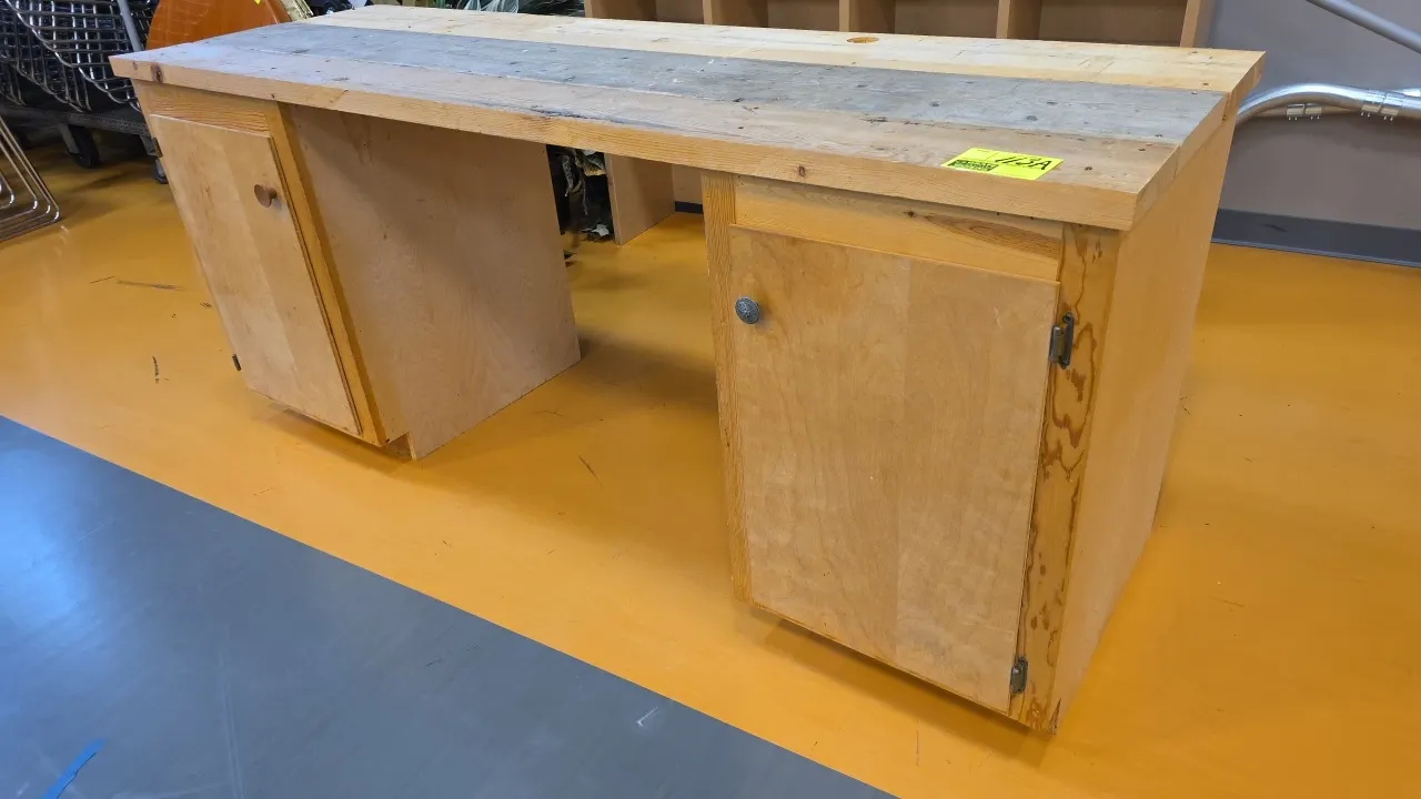 Wood workbench. Features a solid plank wood top with cable passthrough hole, dual single-door pedestal storage cabinets, and open knee space. Dimensio
