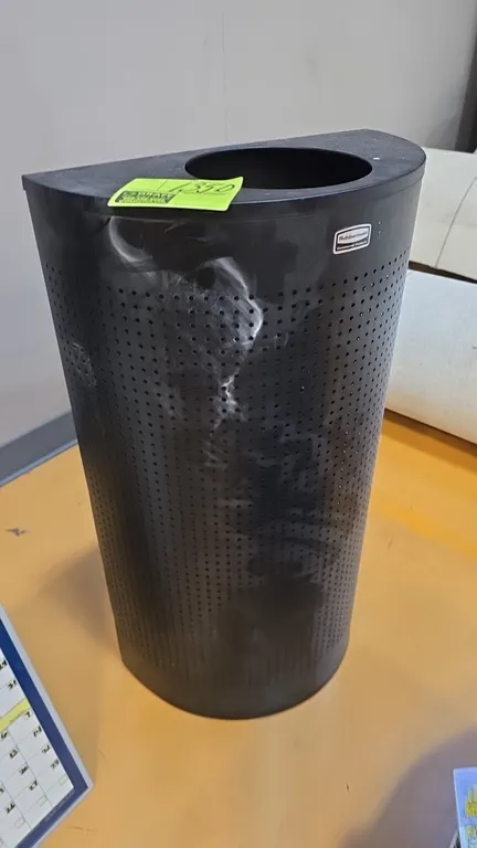 Rubbermaid metal half-round trash can cover. Features perforated metal front, flat back for wall placement, and top circular drop-in opening. Finished