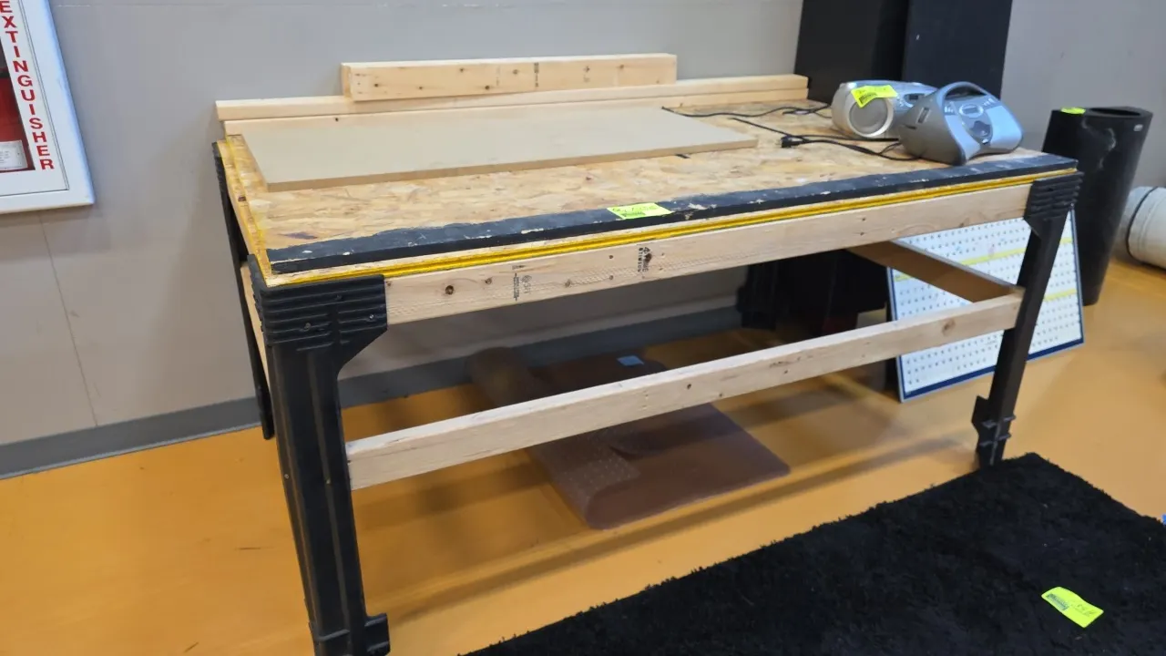 Wood workbench table. Features 2x4 lumber frame construction, molded corner bracket legs, and a Norbord OSB work surface. Includes extra 2x4 lumber pi