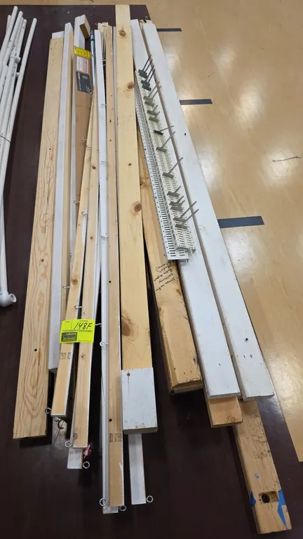 Assorted lumber and wood boards. Includes various lengths and dimensions of unfinished and painted boards, trim, an extension pole, and a pegboard hoo