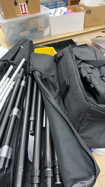 Assorted banner stand parts and hardware. Includes telescoping metal poles with twist-lock collars, crossbar/upright sections, and base plates. Accomp