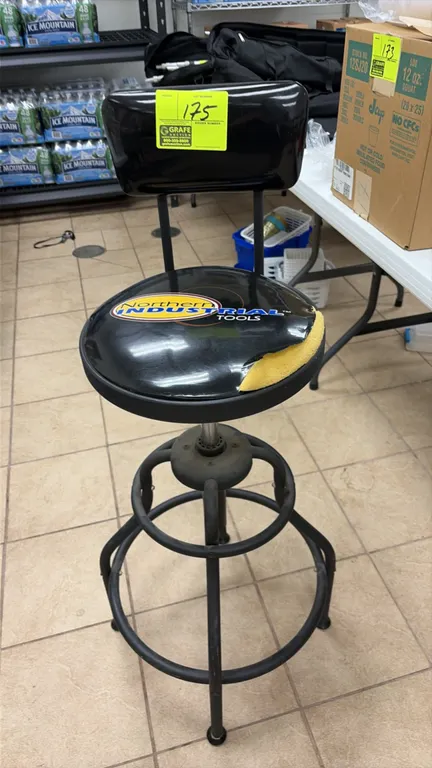 Northern Industrial Tools shop stool with backrest. Features padded vinyl swivel seat, integrated footrest ring, and black tubular metal frame. Note:
