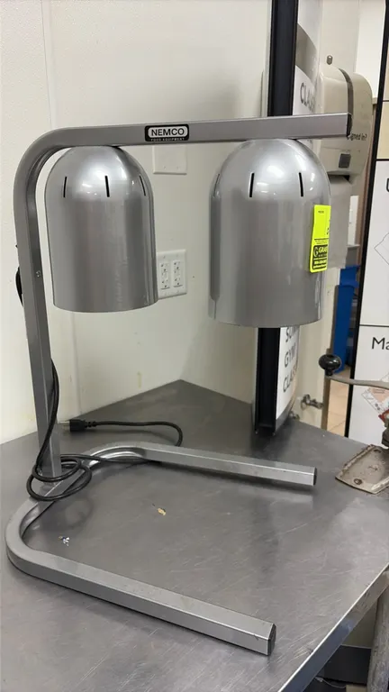 Nemco double-bulb countertop heat lamp. Features two vented aluminum dome shades and a tubular cantilever stand. Includes attached power cord.
