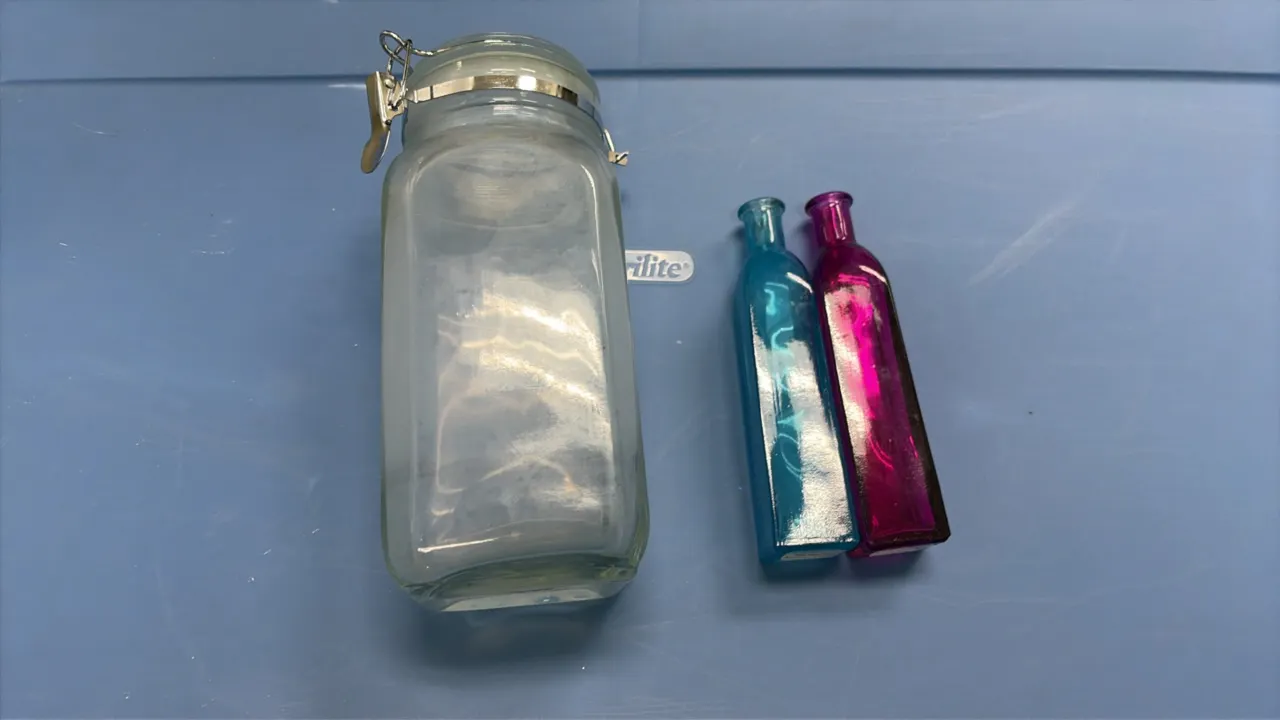 Assorted decor and glassware package lot. Includes a blue plastic storage tote with lid containing packed decorative items, accompanied by a clear gla
