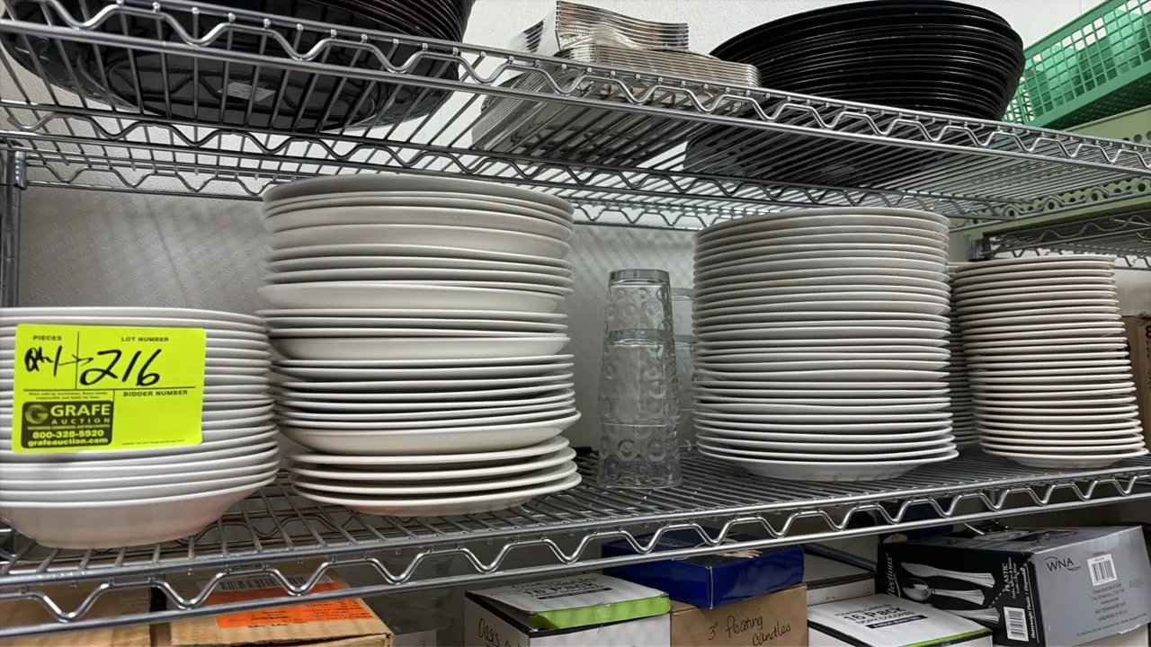 Assorted china plates, bowls, and glassware. Includes white ceramic dinner plates, salad plates, bowls, and clear textured glass tumblers. Wire shelvi