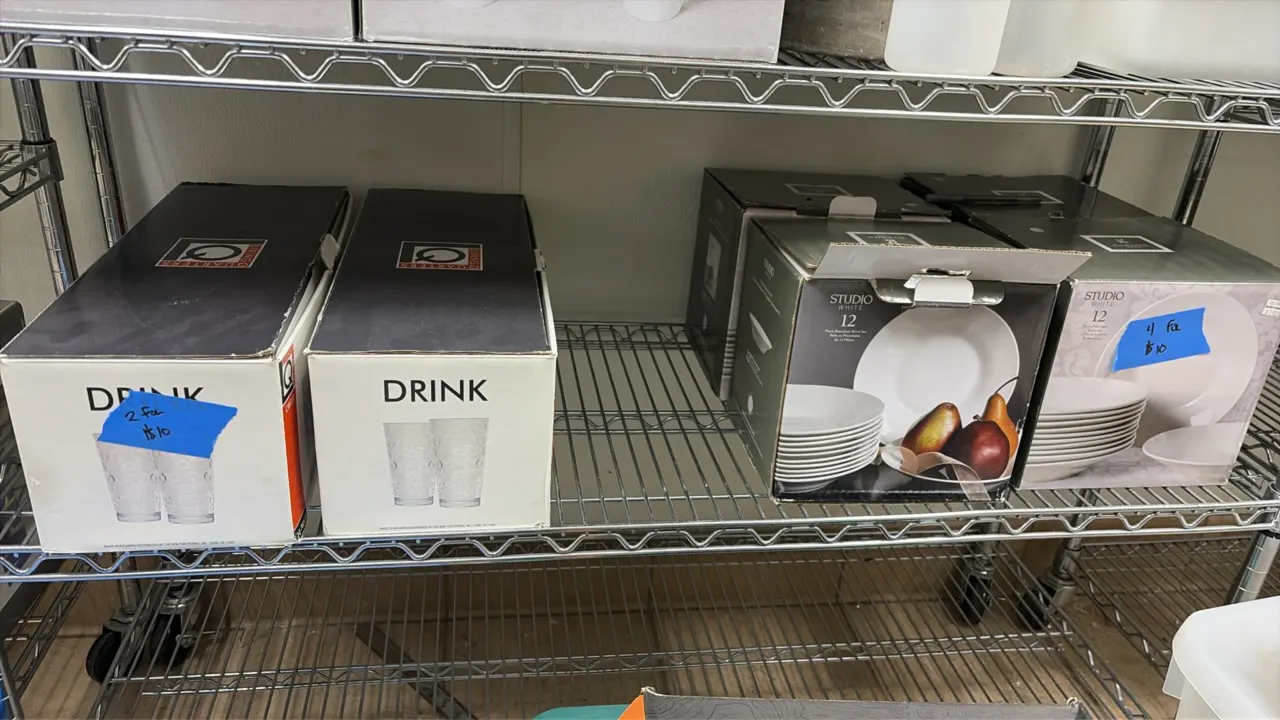 Assorted dinnerware and glassware lot. Includes boxes of Drink glassware sets and Studio White 12 porcelain dinnerware sets. Wire shelving not include