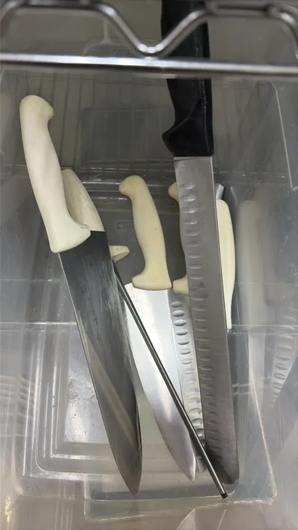 Assorted commercial kitchen knives with sharpening steel. Includes chef knives, granton edge slicers, and a honing steel. Features stainless steel bla