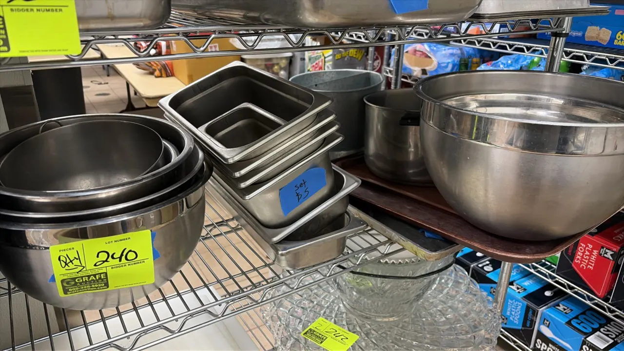Assorted stainless steel kitchenware. Includes nested mixing bowls, fractional steam table pans, a pot, and serving trays. Wire shelving and surroundi