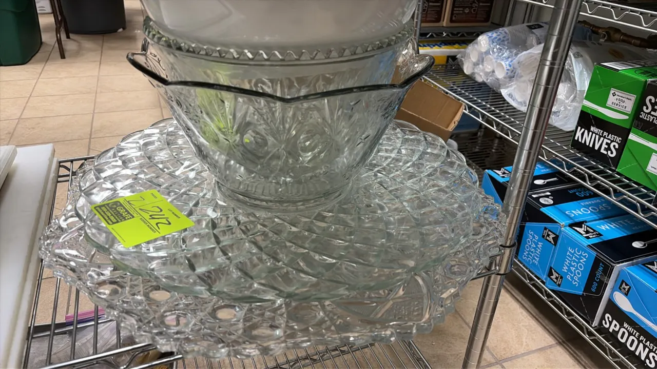 Glass punch bowls and serving trays. Features clear pressed glass construction with decorative diamond-cut pattern and scalloped rims. Shelving and ba