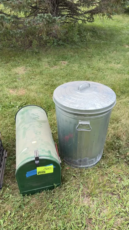 Metal mailbox and galvanized trash can lot. Includes a green painted metal mailbox with latch and red indicator flag, and a galvanized steel trash can