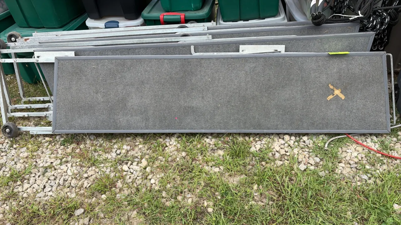 Folding stage risers. Features gray carpeted platform surfaces, collapsible metal frame construction, and integrated wheels for transport.