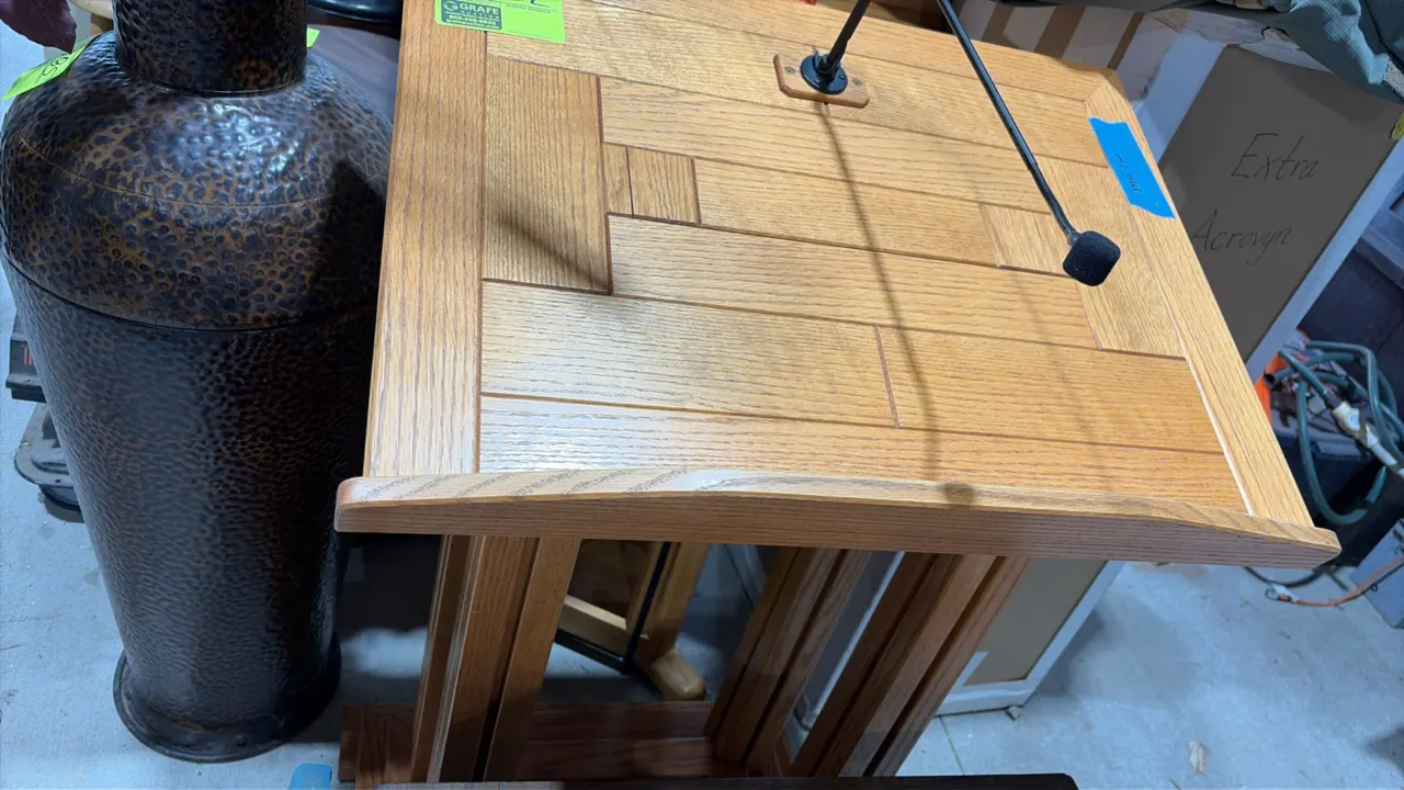 Wood podium. Features oak construction, slanted reading surface with book stop ledge, and integrated gooseneck microphone. Background items not includ