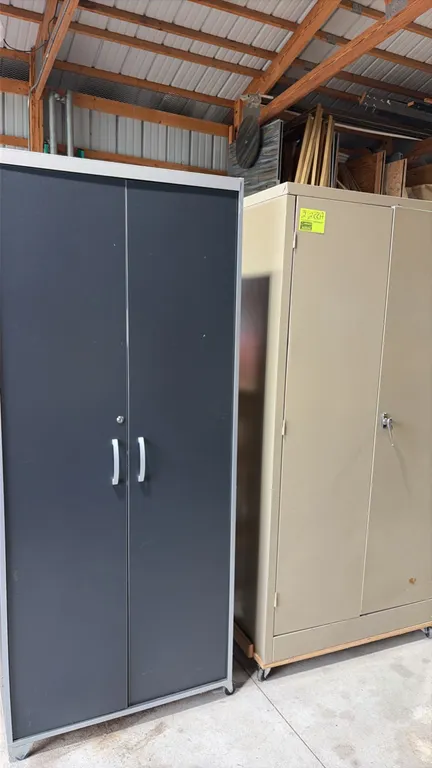 Two-door storage cabinets. Includes (1) tan metal 2-door storage cabinet with locking latch handle and (1) dark gray laminate 2-door storage cabinet w