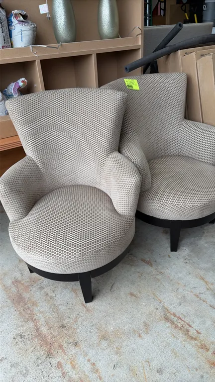 Upholstered lounge chairs. Features tan patterned fabric upholstery, flared backs, integrated armrests, and rounded seats. Supported by dark-finished
