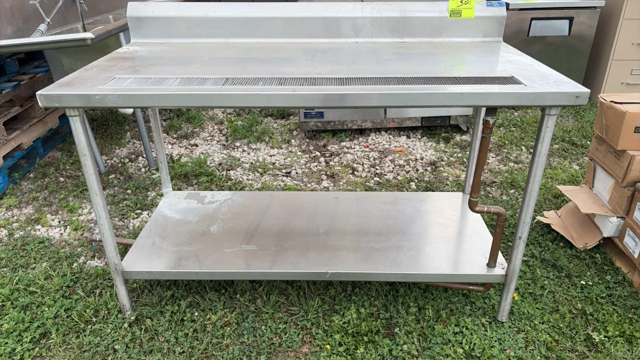 Stainless steel work table. Features a backsplash, integrated slotted drain trough with copper drain pipe, and undershelf. Dimensions: 60" x 30". Moun