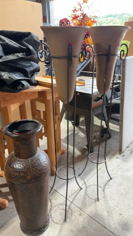 Decorative floor vases. Includes two tall tapered vases mounted in black metal tripod stands with scroll accents, and one textured brown floor urn.