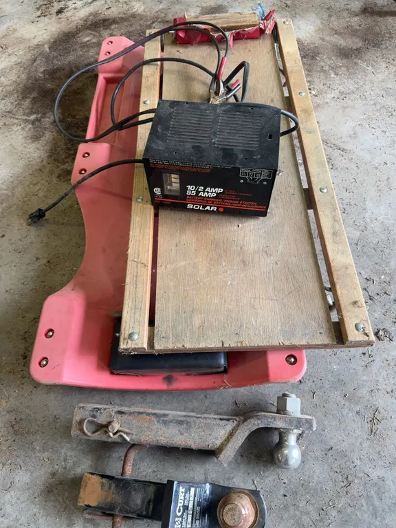 Automotive Accessory Lot With Battery Charger, Curt Hitch, Fuel Cans, Creeper, And Cables