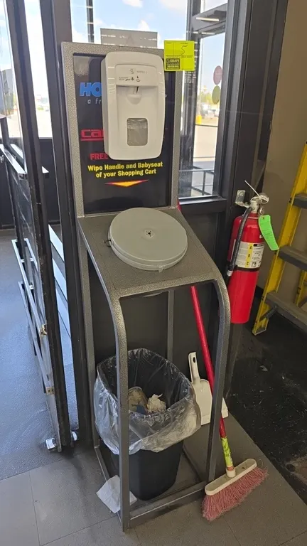 Metal sanitation station stand. Features Triple S automatic hand sanitizer dispenser, wipe dispenser compartment, and lower shelf with trash can. 58"H