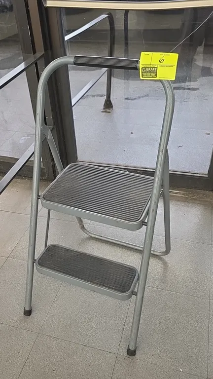 2-step folding metal step stool. Features a tubular metal frame, 2 ribbed slip-resistant step treads, top hand grip, and rubber feet.