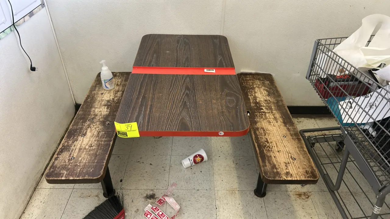 Picnic table with attached bench seating. Features a woodgrain laminate tabletop with red edge trim and two attached bench seats. Mounted on a black m