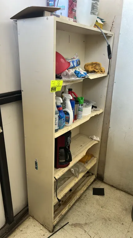 Laminate shelving unit with contents. Includes Mr. Coffee maker, handheld pump sprayer, cleaning supplies, soap refill bags, and remaining contents. F