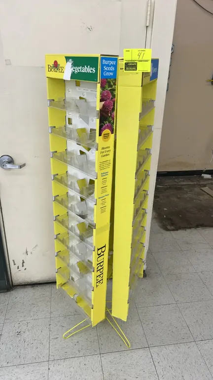 Burpee 3-sided rotating seed packet merchandiser. Features multi-tier clear plastic packet display pockets and Burpee branded graphics. Mounted on a r