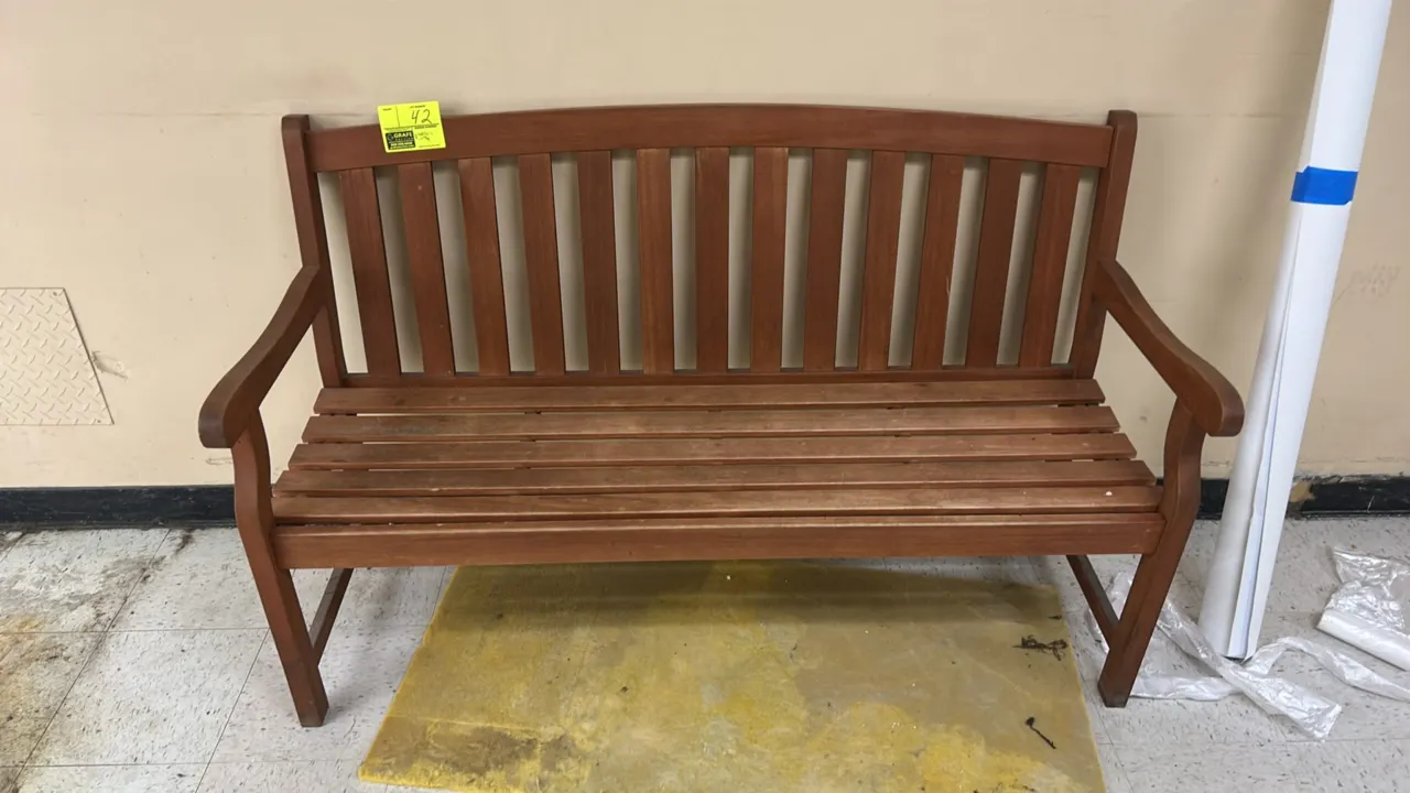 Wooden bench. Features a slatted seat, vertical slat back with arched top rail, and integrated armrests. 5'L.