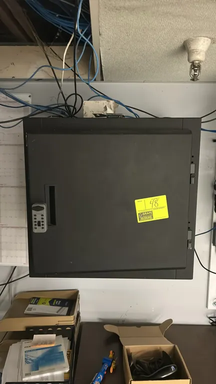 Metal wall-mounted IT cabinet. Features a single front door with a push-button combination lock, side latch with padlock, and internal equipment rack