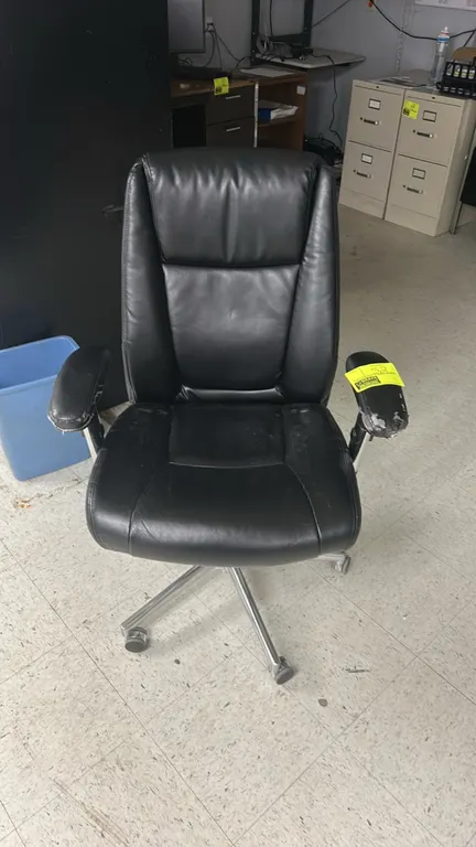 Executive office chair. Features black cushioned upholstery, high back, and adjustable armrests. Mounted on a chrome 5-star base with casters. Note: A