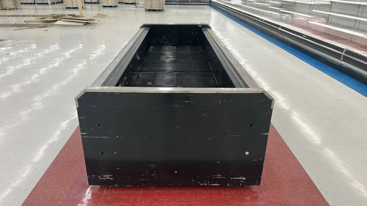 Hussmann self-contained wide island display case. Features an open-top design, stainless steel perimeter rail trim, and black wire bottom rack decking