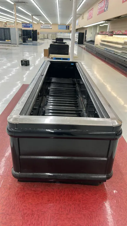 Hussmann self-contained island display case. Features stainless steel top rail trim, protective black bumpers, and black slotted interior deck pans. D