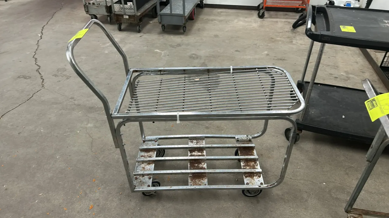 Metal 2-tier utility cart. Features upper wire shelf, lower slatted deck, and integrated push handle. 3'L. Mounted on casters.