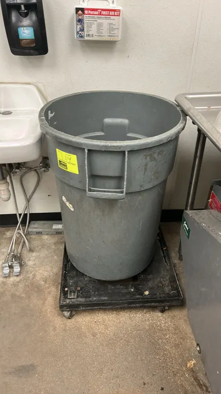 Poly trash bin with mobile cart base. Features gray plastic construction and integrated side handles. Mounted on a black rectangular mobile cart base