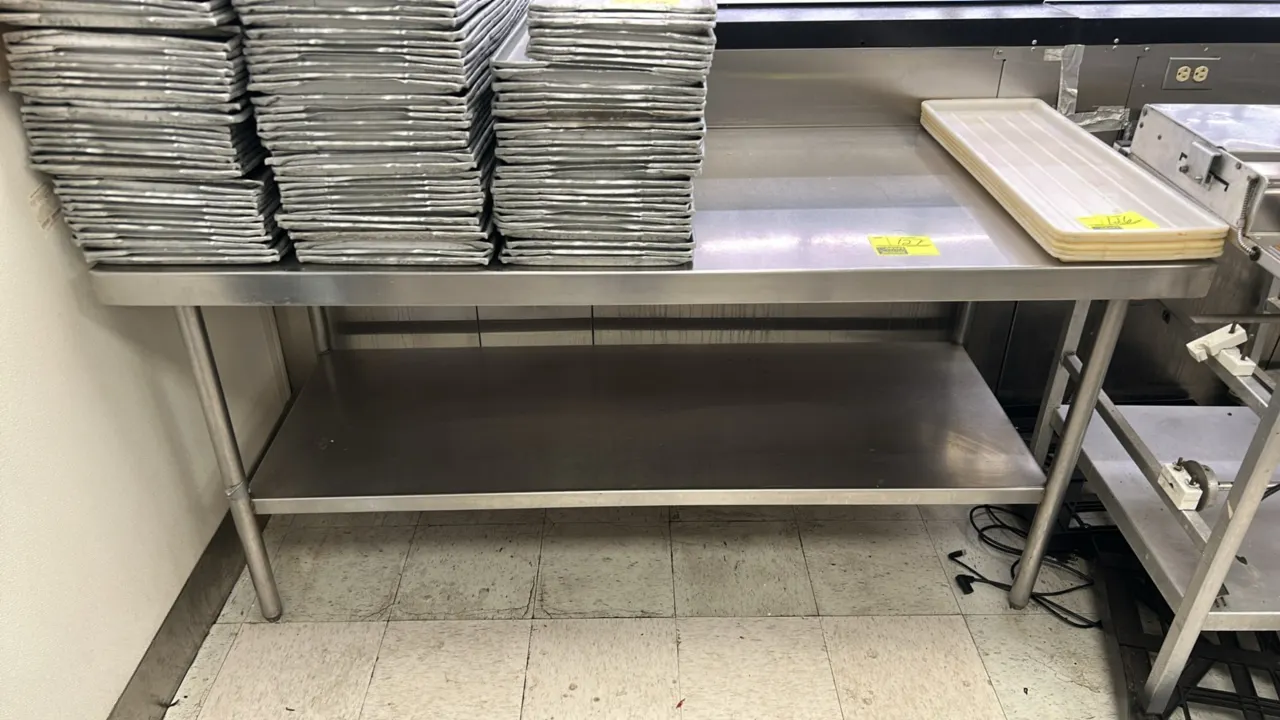 Stainless steel work table. Features a flat top and lower undershelf. Mounted on tubular metal legs with adjustable bullet feet. 72"L x 30"W. Contents