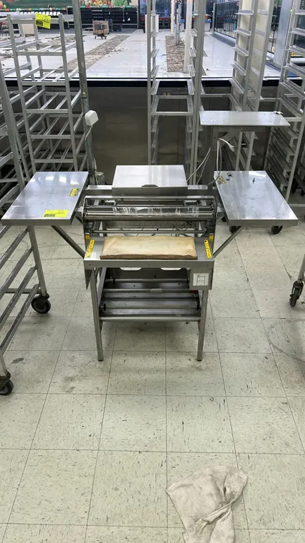 Stainless steel commercial wrapping station. Features a heated seal pad, film cradle rollers, dual stainless steel side extension shelves, upper scale