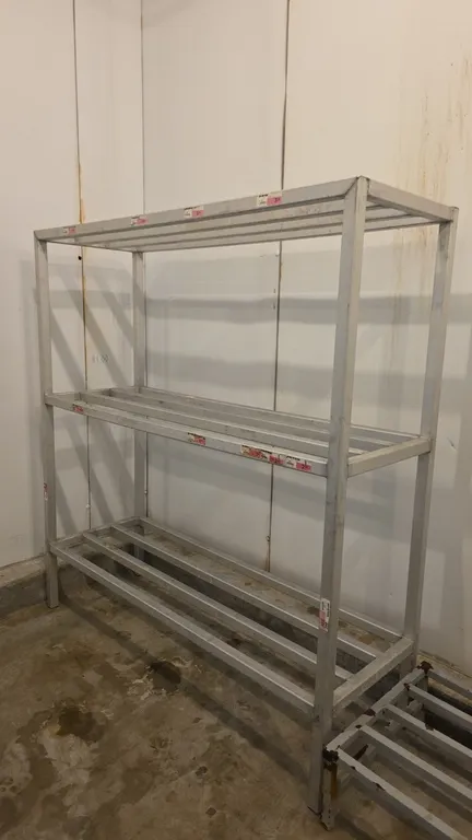 Aluminum 3-tier storage rack. Features welded tubular aluminum construction and slatted shelf tiers. 5'L x 1'8"W x 5'4"H.