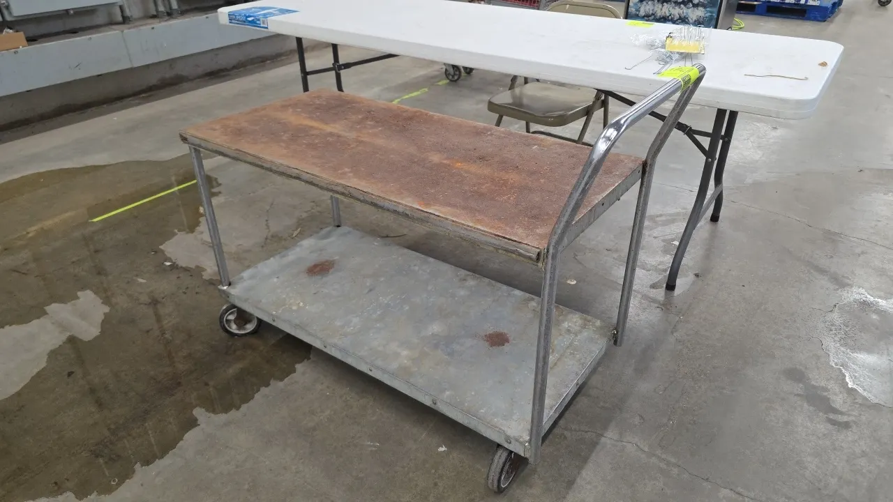 Metal 2-tier cart. Features two solid shelves and an integrated tubular push handle. 42"L. Mounted on casters. Note: Heavy rust on top shelf.