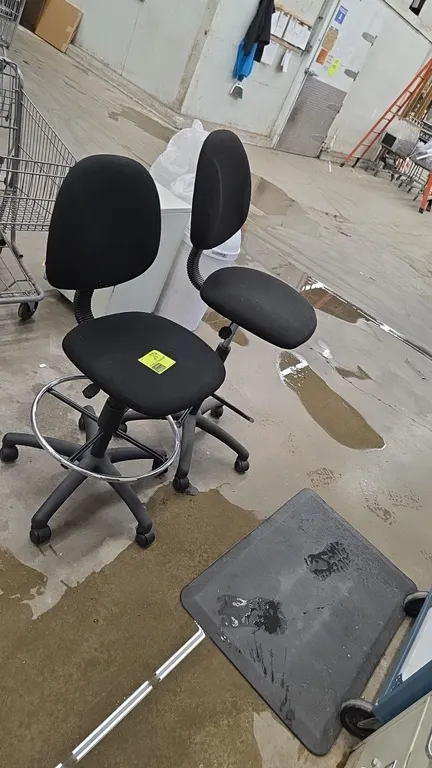 Adjustable cushioned office drafting chairs with anti-fatigue floor mat. Features black fabric upholstery, pneumatic height adjustment, and chrome foo