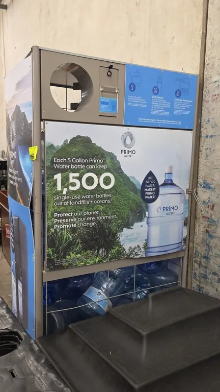 Primo metal water merchandiser. Features upper bottle return drop chute, branded graphic panels, and wire grid enclosure. Designed for 3- and 5-gallon